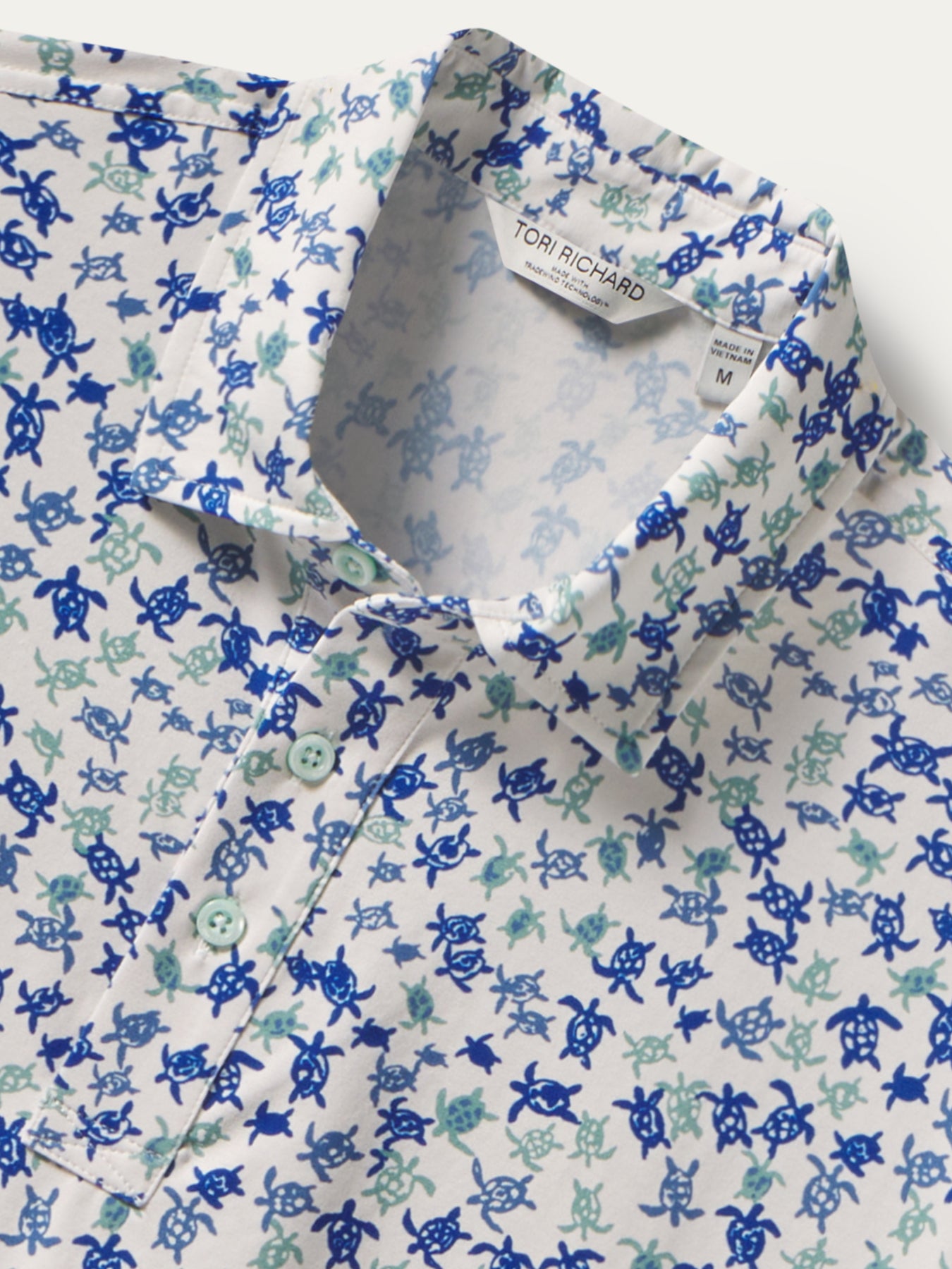 Blue and teal honu-pattern short-sleeve polo shirt, front view with label, and close-up of fabric and branding.