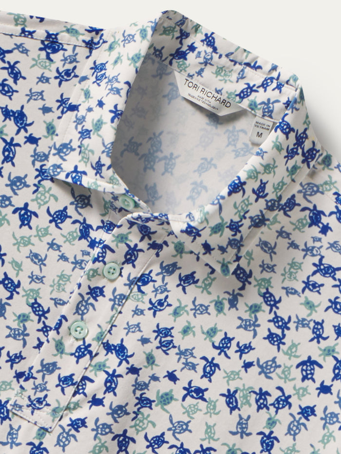 Blue and teal honu-pattern short-sleeve polo shirt, front view with label, and close-up of fabric and branding.