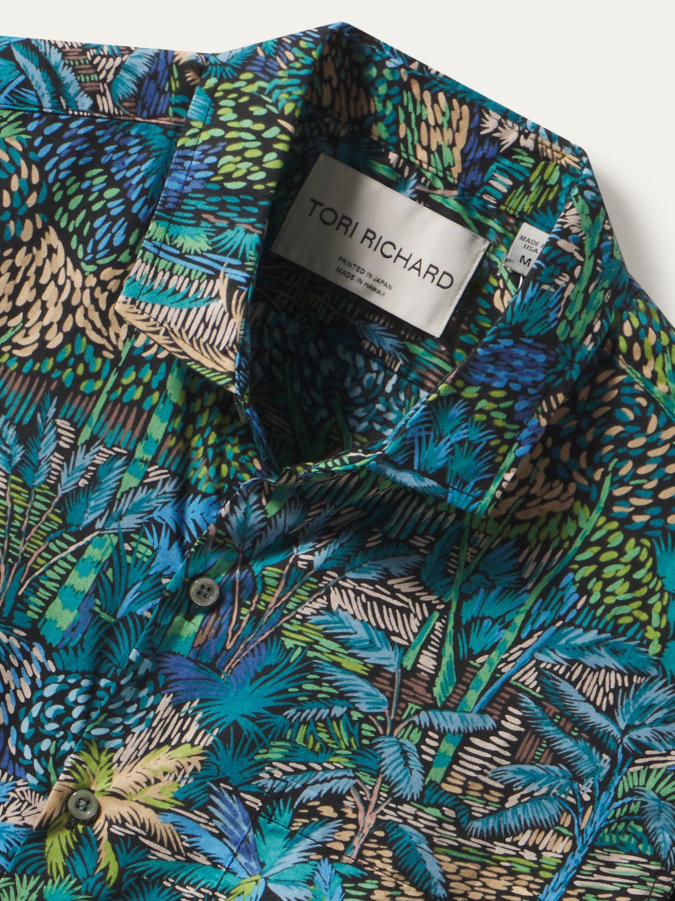 Green and blue tropical-leaf print cotton shirt, fabric detail close-up.