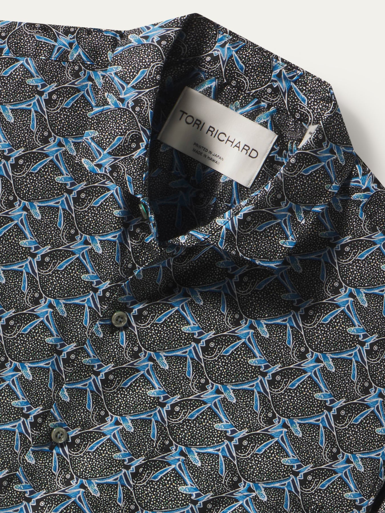 Close-up of a patterned button-up shirt collar with a visible Tori Richard label. The fabric has a black base with dense small white dots and an allover blue abstract leaf or branch motif.