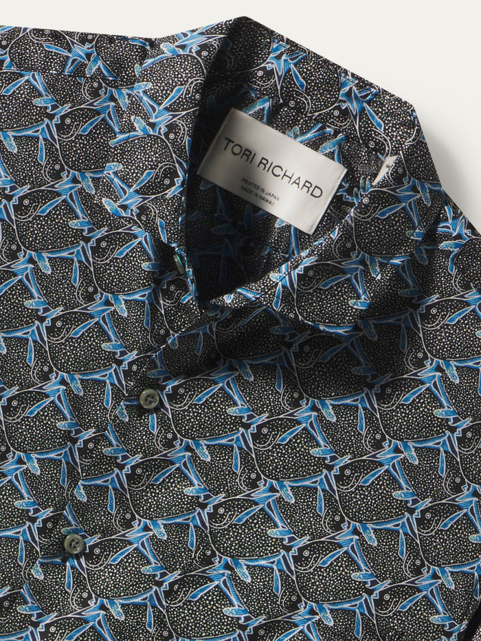 Close-up of a patterned button-up shirt collar with a visible Tori Richard label. The fabric has a black base with dense small white dots and an allover blue abstract leaf or branch motif.