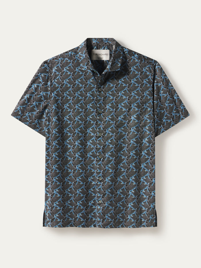 A short-sleeve button-up shirt with a dark gray and black background covered in a repeating light blue graphic pattern, displayed flat against a light off-white background.