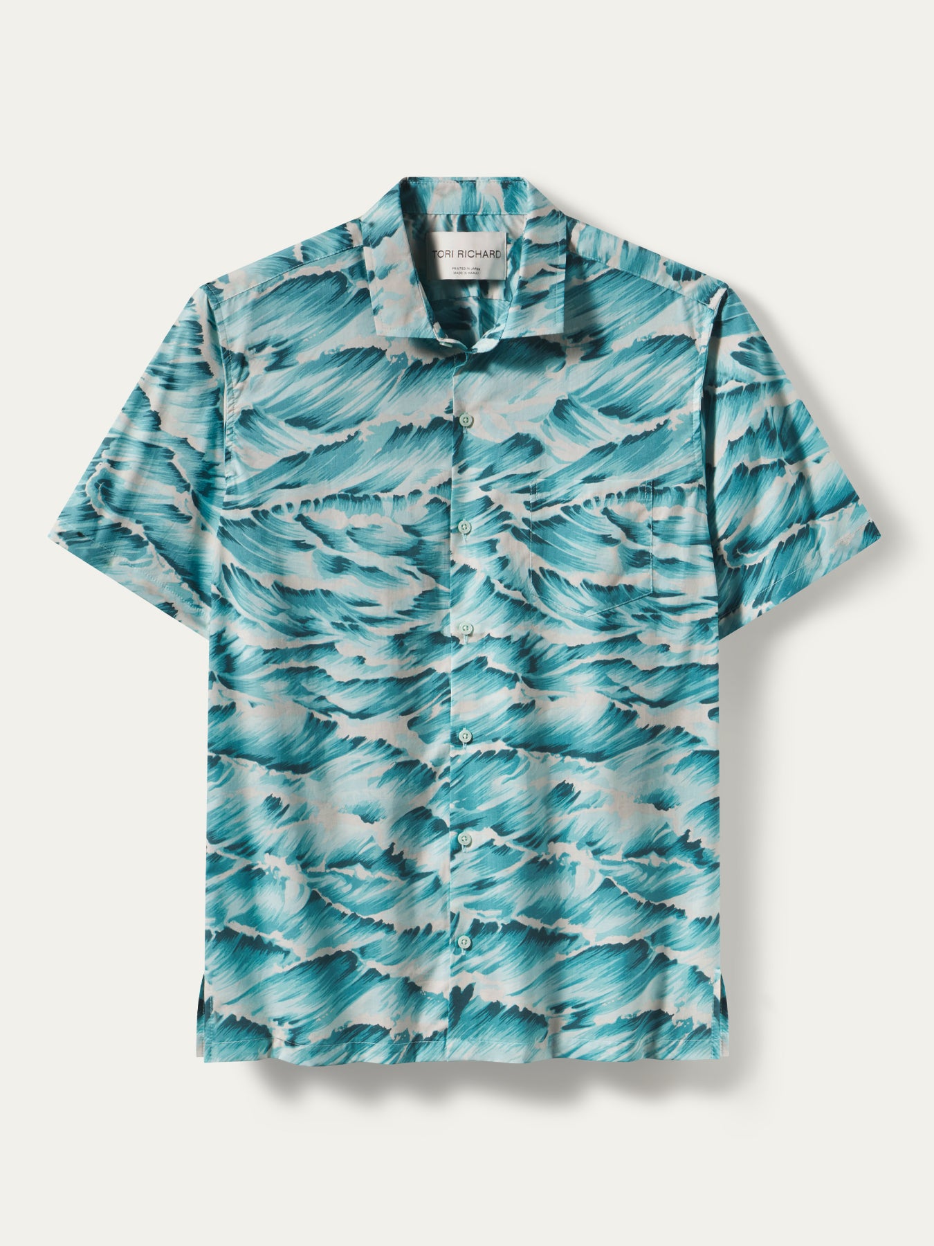 A short-sleeve button-up camp shirt with an all-over teal and white wave print, displayed flat against a light beige background.