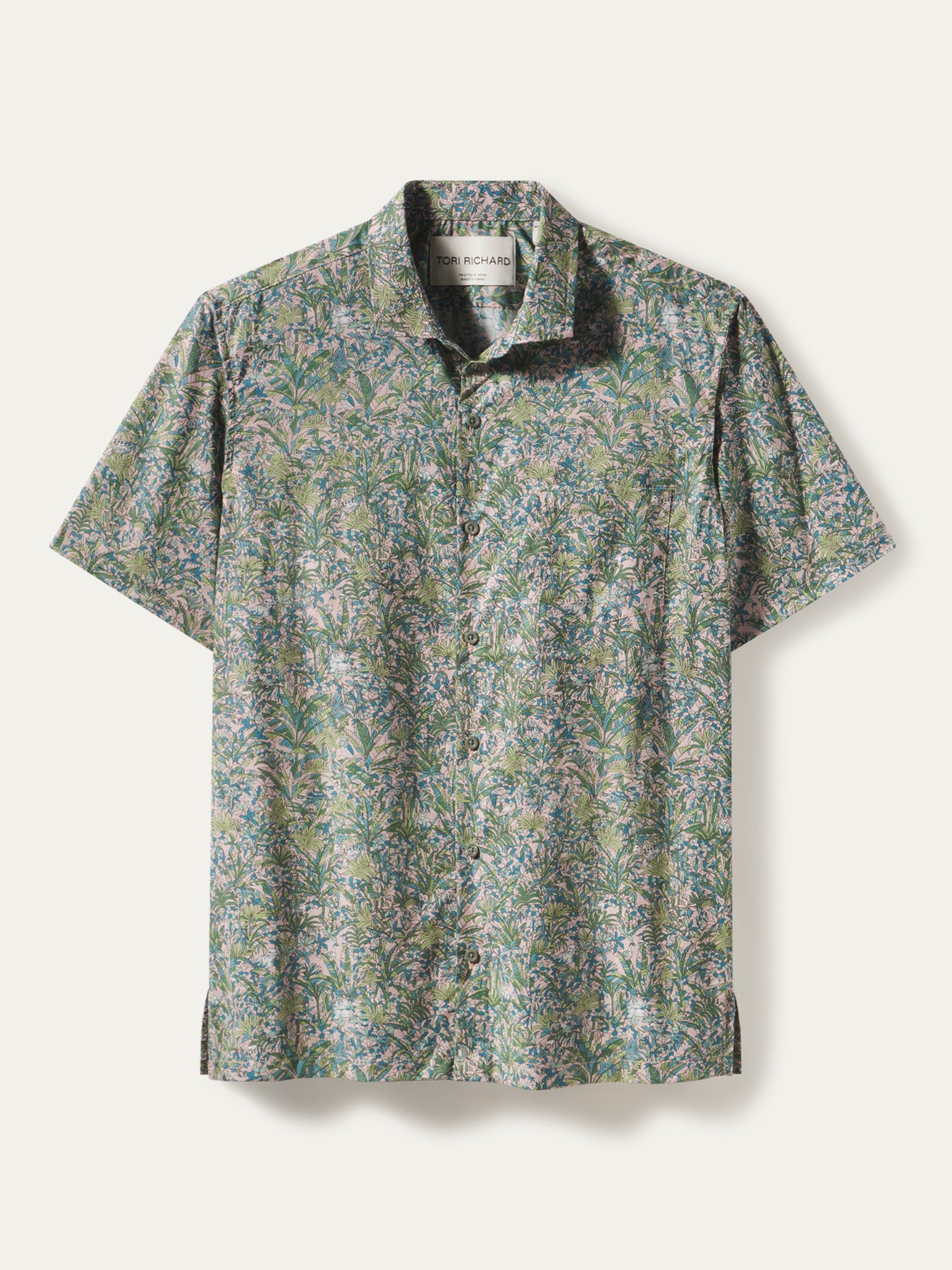 White short-sleeve shirt with green and purple leaf print; white cotton Hawaiian shirt, leaf pattern, flat lay.