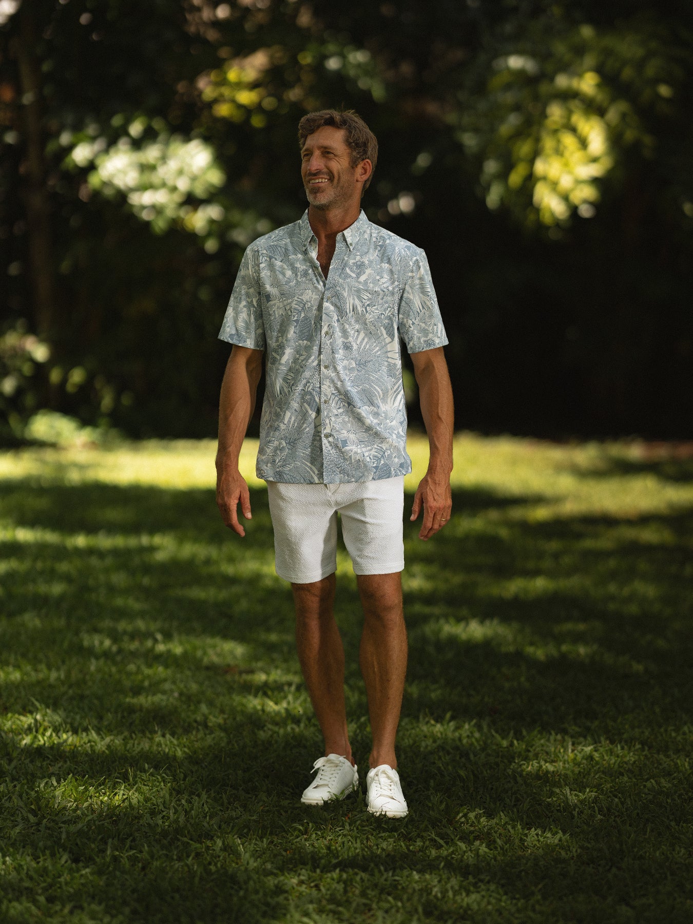 Green/blue leafy-print Tradewind Technology® shirt with white shorts, full-body outdoor view.
