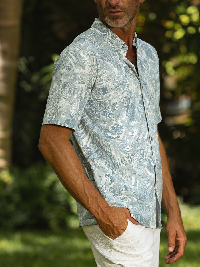 Green tropical-print short-sleeve shirt and white pants, front view outdoors, hand in pocket.
