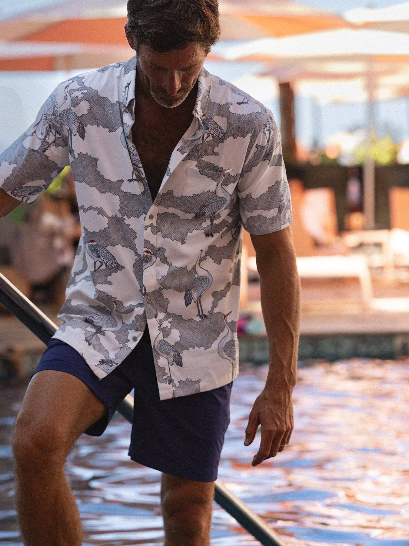 White and blue patterned short-sleeve shirt with blue shorts, poolside side view.
