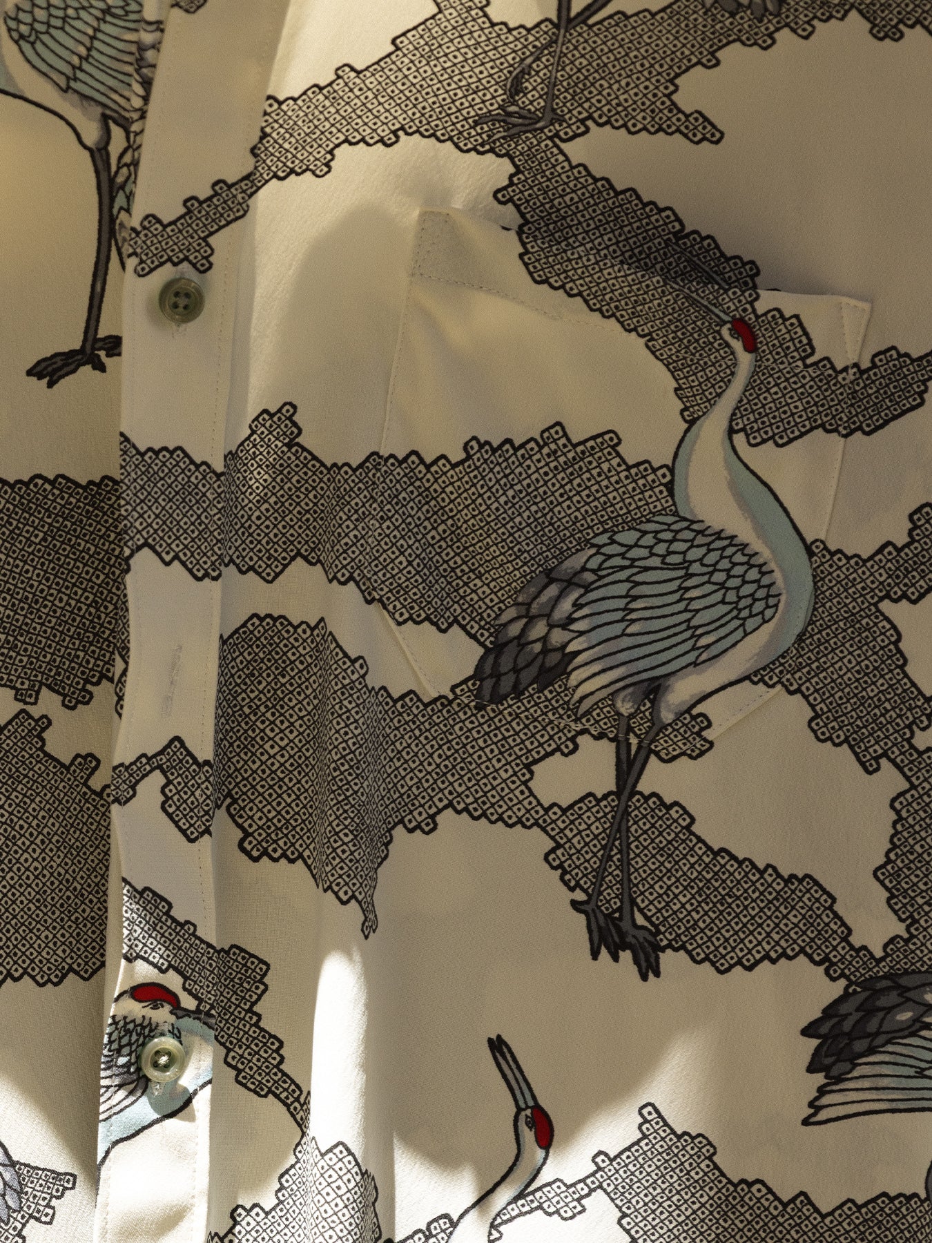 White crane and cloud-print shirt, close-up of buttons, pocket, and vintage/traditional artwork.