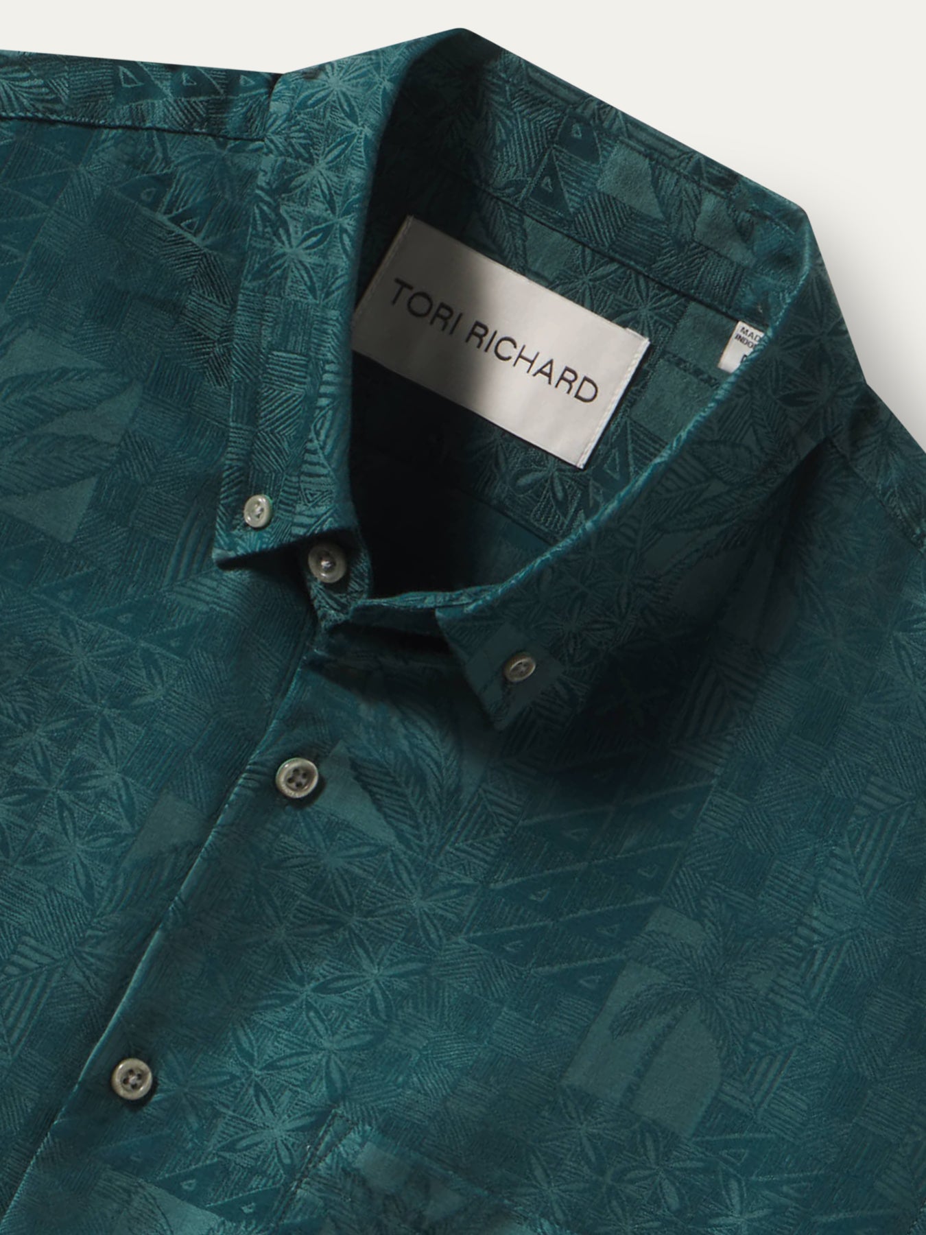 Close-up of a teal patterned button-down shirt by Tori Richard, showing the collar label and front buttons against a light neutral background.
