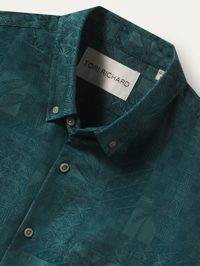 Close-up of a teal patterned button-down shirt by Tori Richard, showing the collar label and front buttons against a light neutral background.