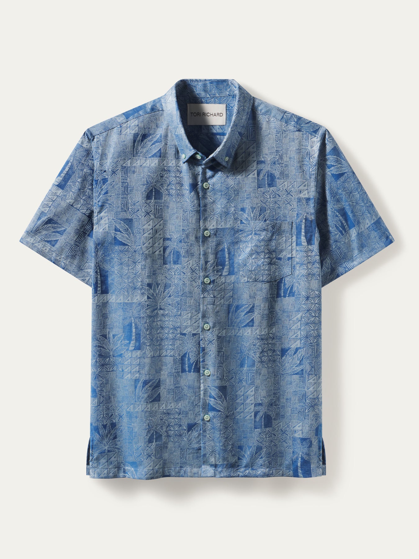A short-sleeve button-up shirt in a textured blue and white tropical leaf pattern, displayed flat against a light cream background.