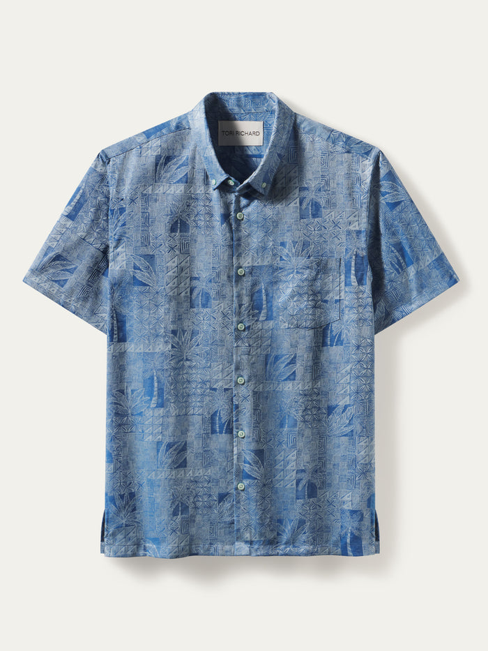 A short-sleeve button-up shirt in a textured blue and white tropical leaf pattern, displayed flat against a light cream background.