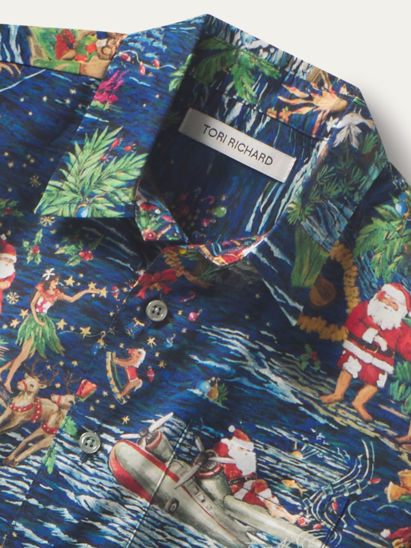 Blue shirt with Santa, hula dancers, and boat print, short sleeves, front view shown in both images.