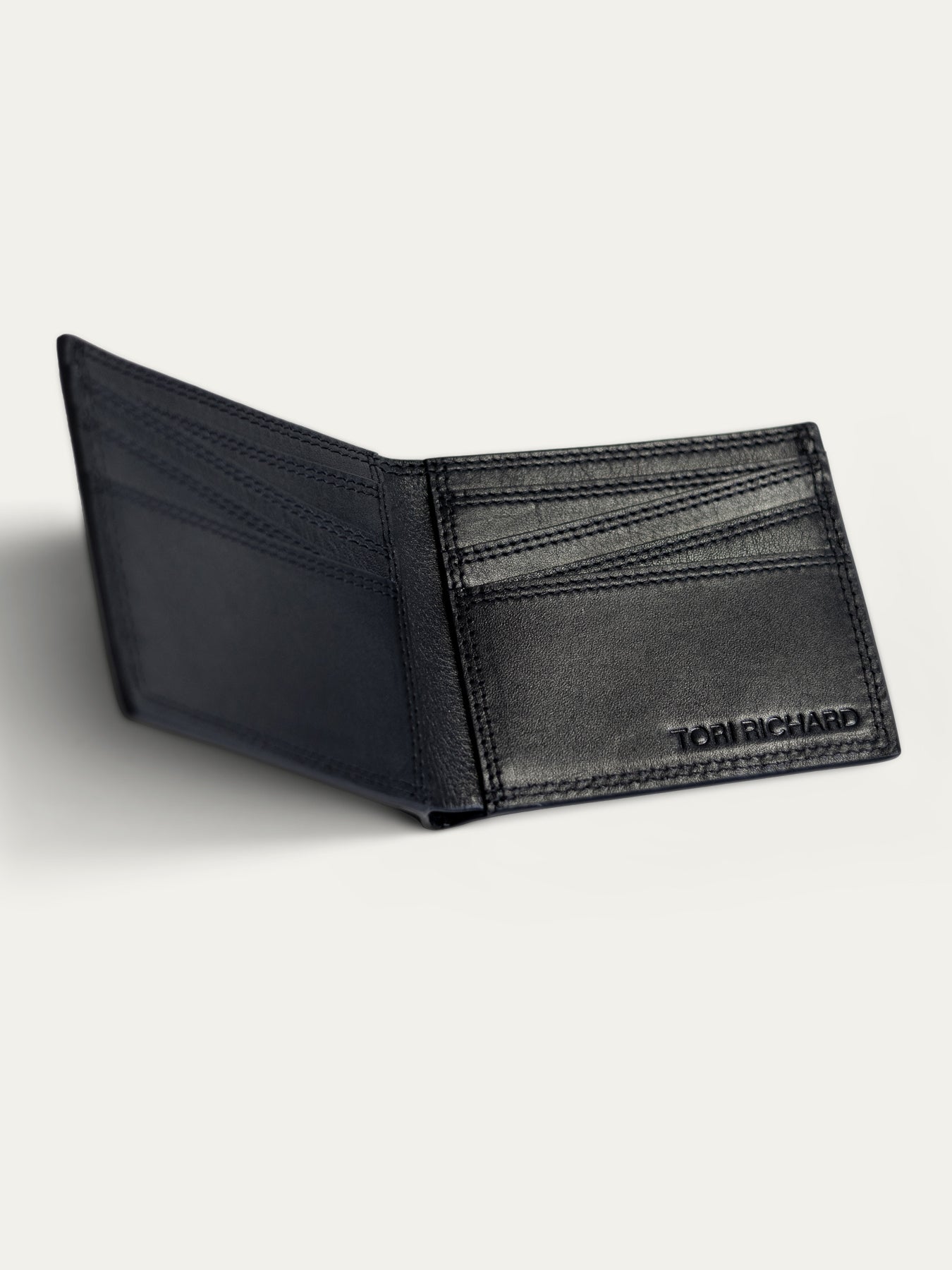 A black leather bi-fold wallet shown open, displaying its interior card slots and the debossed brand name 'TOM RICHARD' on the right side, set against a light gray background.