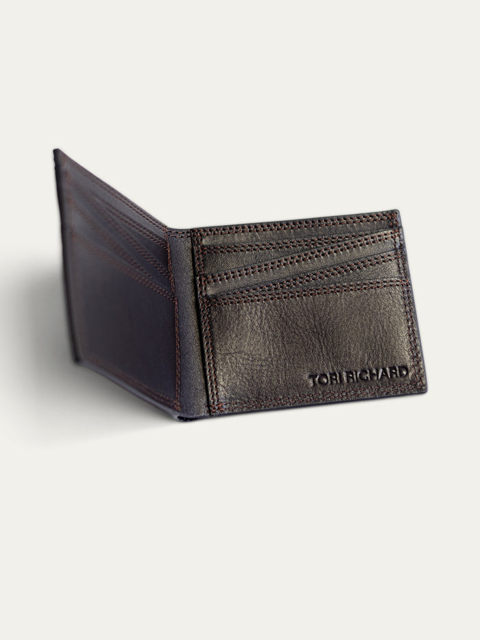 A dark brown leather bi-fold wallet shown open, featuring card slots on the front and the debossed brand name 'TORI RICHARD' on the lower right corner, set against a light off-white background.
