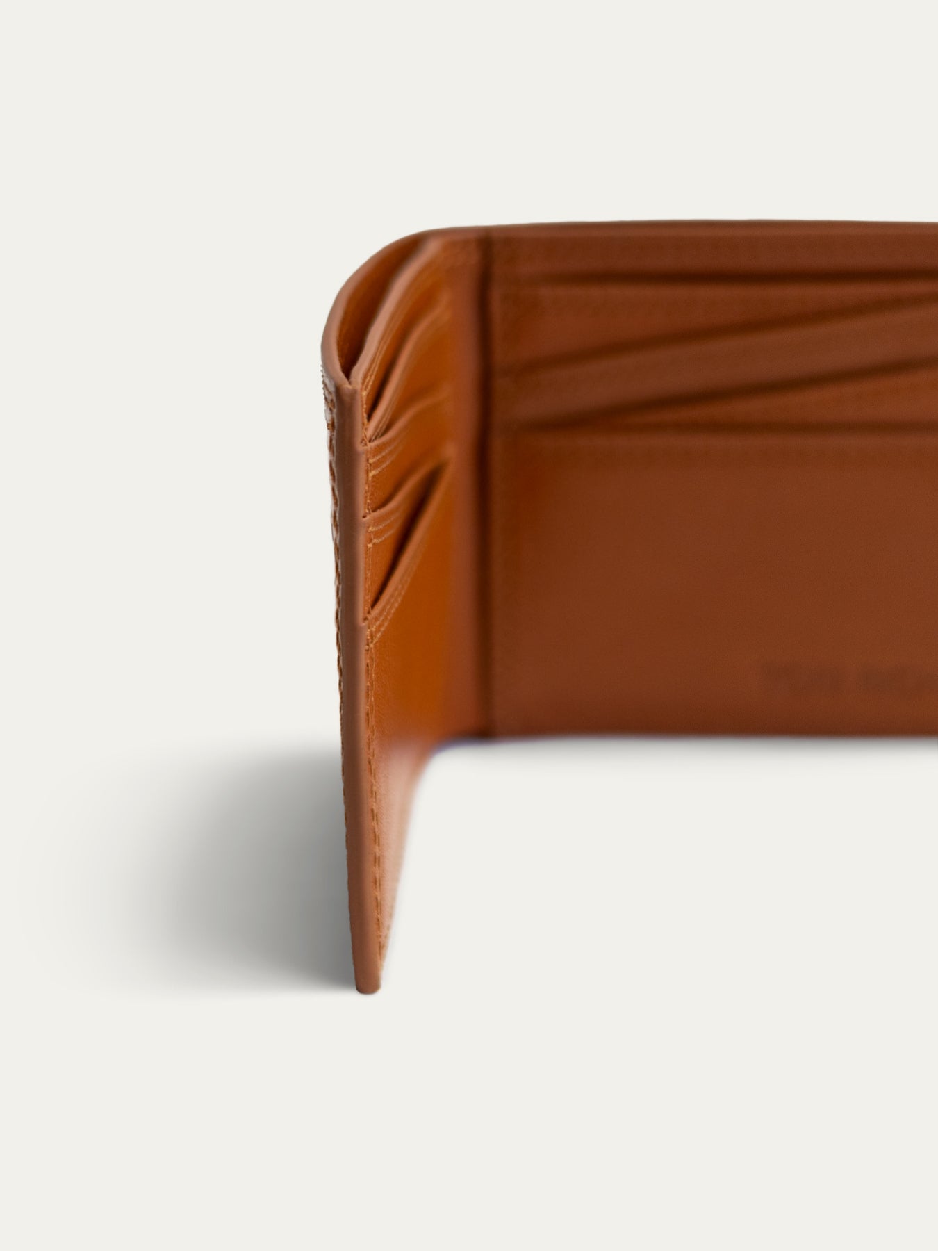 Close-up of a warm brown leather wallet corner showing card slots and interior stitching on a light gray background.