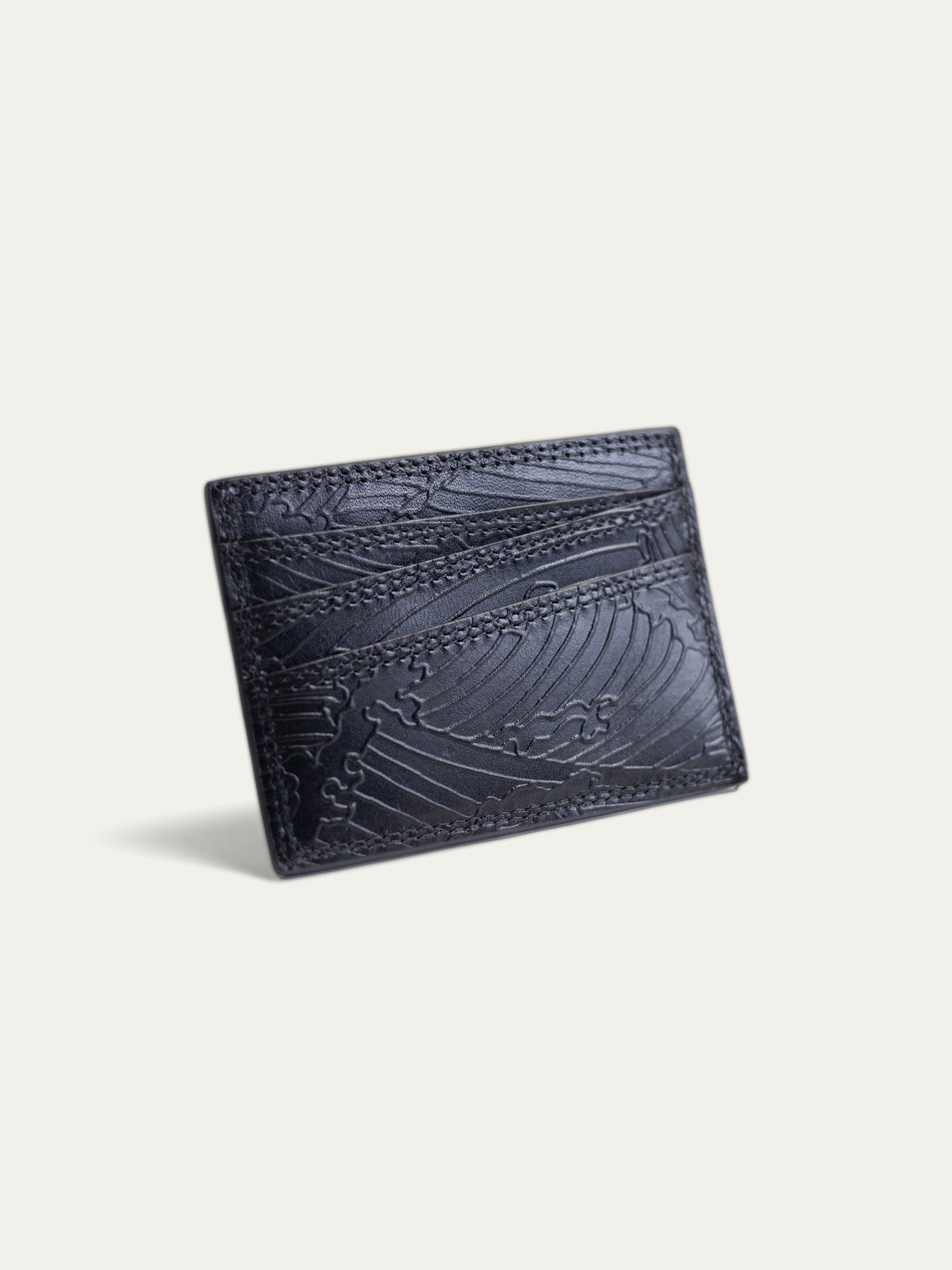 A black leather cardholder wallet with an embossed wave pattern, shown at an angle on a light off-white background.