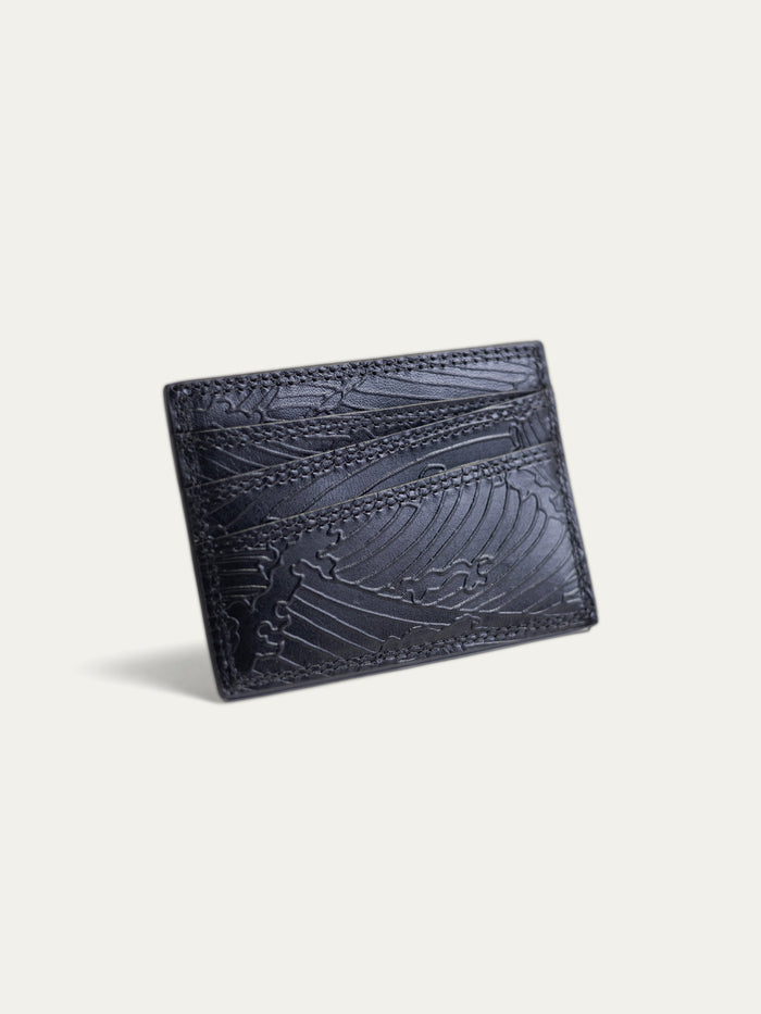A black leather cardholder wallet with an embossed wave pattern, shown at an angle on a light off-white background.