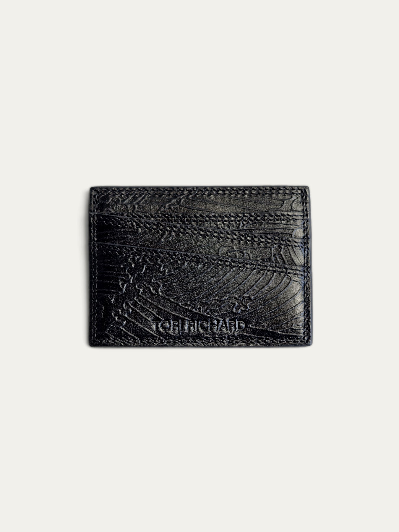 A black textured leather card holder wallet with an embossed pattern and the brand name 'TCH RICHARD' debossed near the bottom, shown on a light off-white background.