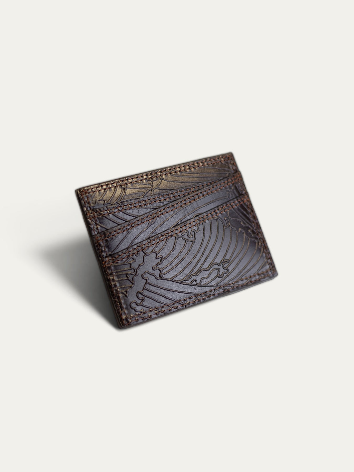A dark brown leather card holder wallet with embossed wave patterns and contrast stitching, shown on a light off-white background.