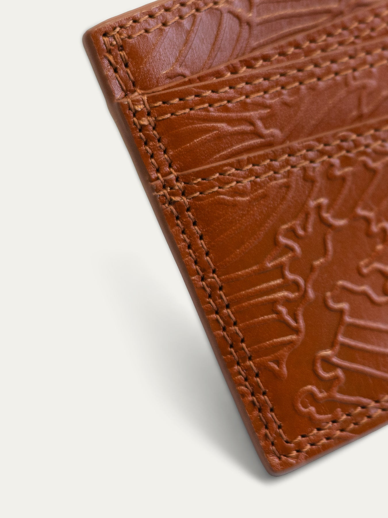Close-up of a brown embossed leather card holder or wallet corner with visible stitching on a light gray background.