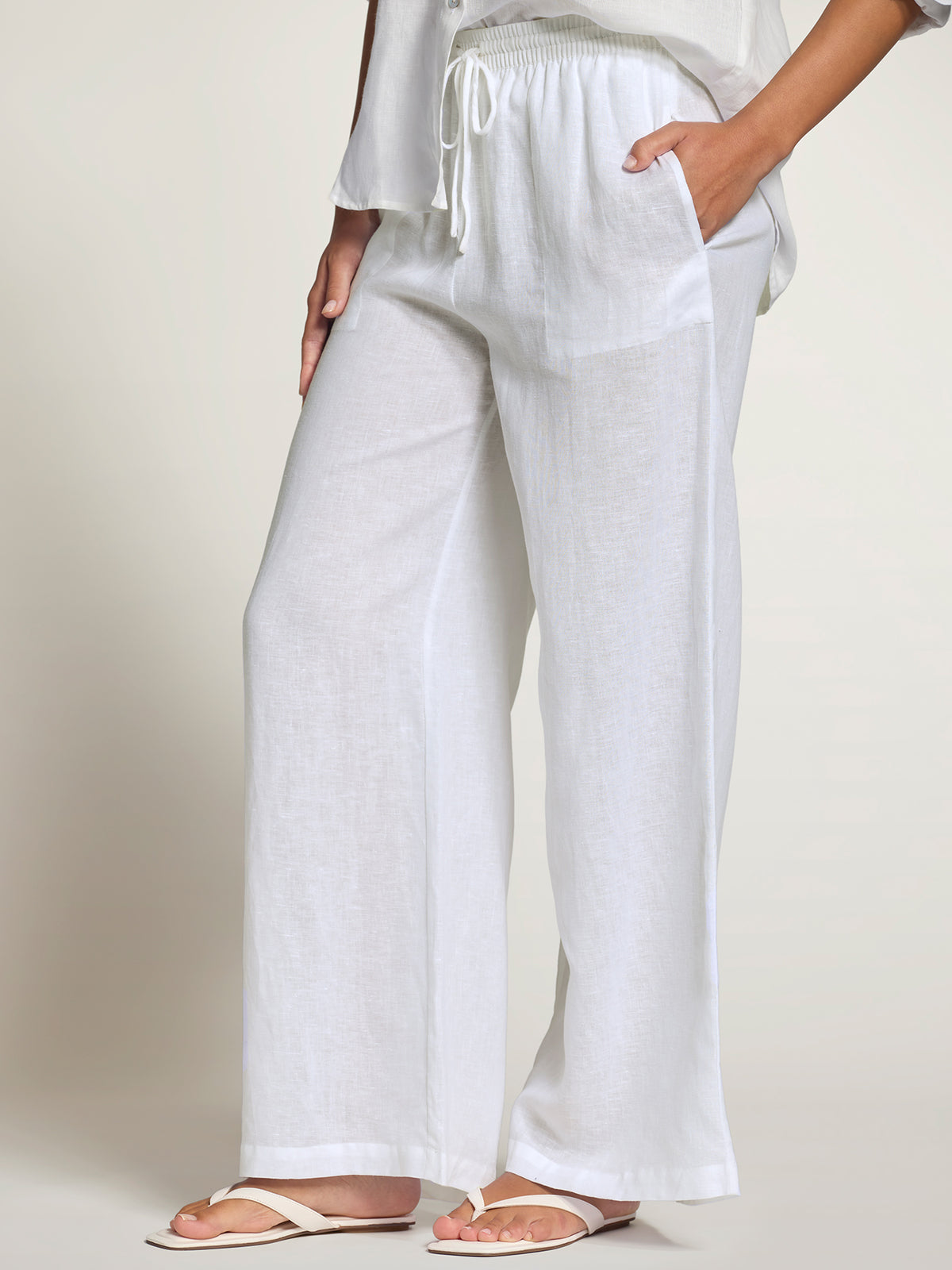 White linen pants with drawstring waist and pockets, shown in full front view.
