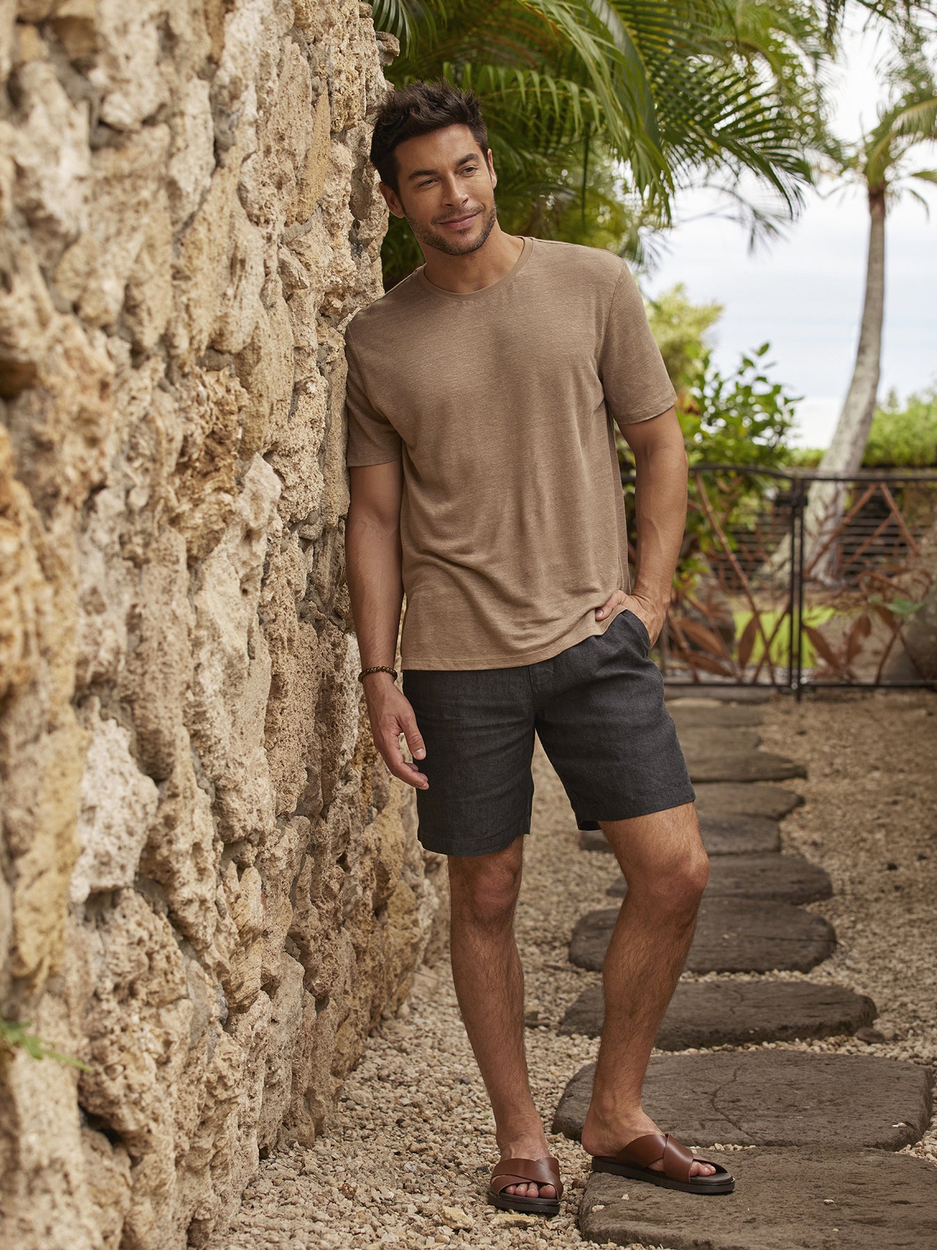 Tan linen shirt and matching Baja Linen Shorts, side view by stone wall and tropical plants.