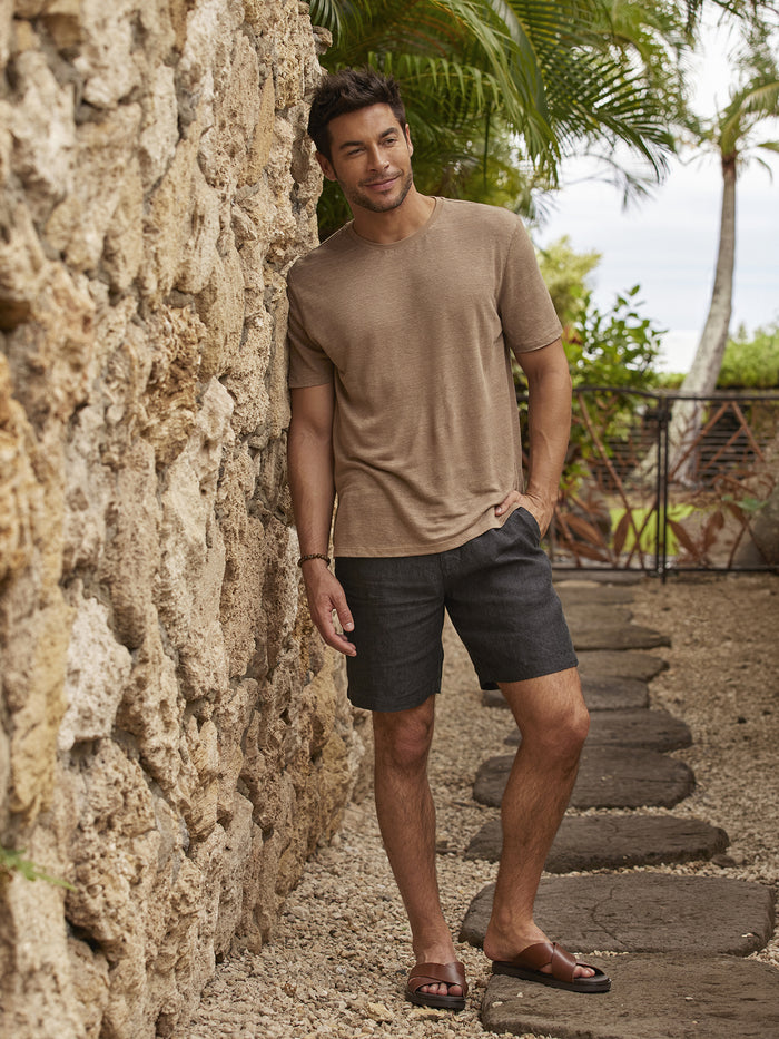 Tan linen shirt and matching Baja Linen Shorts, side view by stone wall and tropical plants.