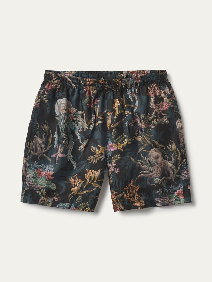 A pair of men's swim shorts featuring an all-over underwater print with sea creatures like octopuses, jellyfish, and a shark, set against a dark teal background with gold, pink, and green details. The shorts have an elastic waistband and are displayed flat against a light off-white background.