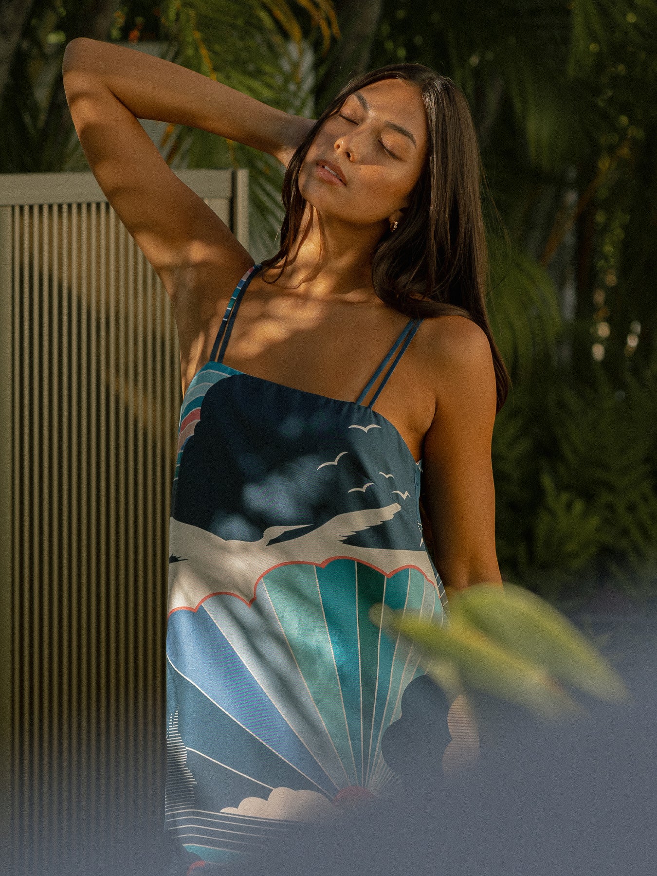 Blue silk twill dress with bird and wave print; model outdoors with arm raised, eyes closed.