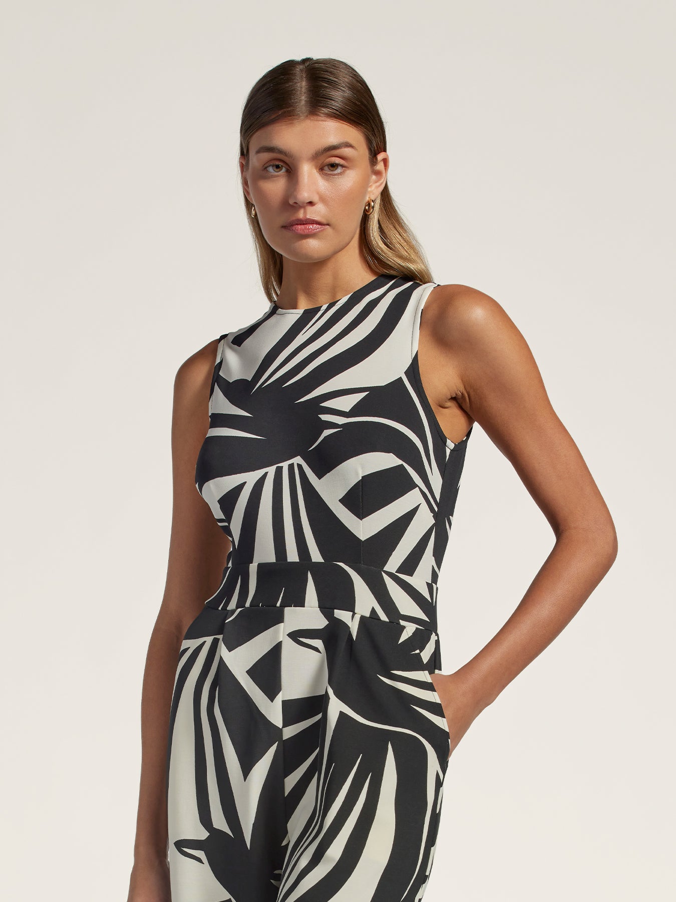 Black sleeveless jumpsuit with jeweled neckline, one hand in pocket, front view.