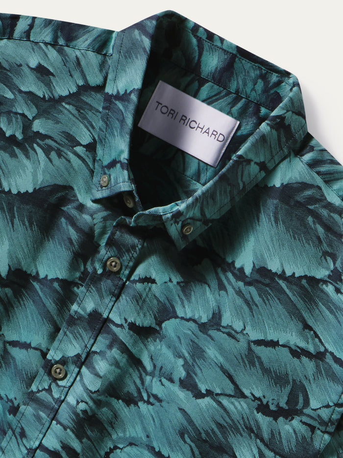 A close-up of a Tori Richard button-down shirt featuring a dark teal and black abstract leaf-like pattern, with a silver brand label visible inside the collar.
