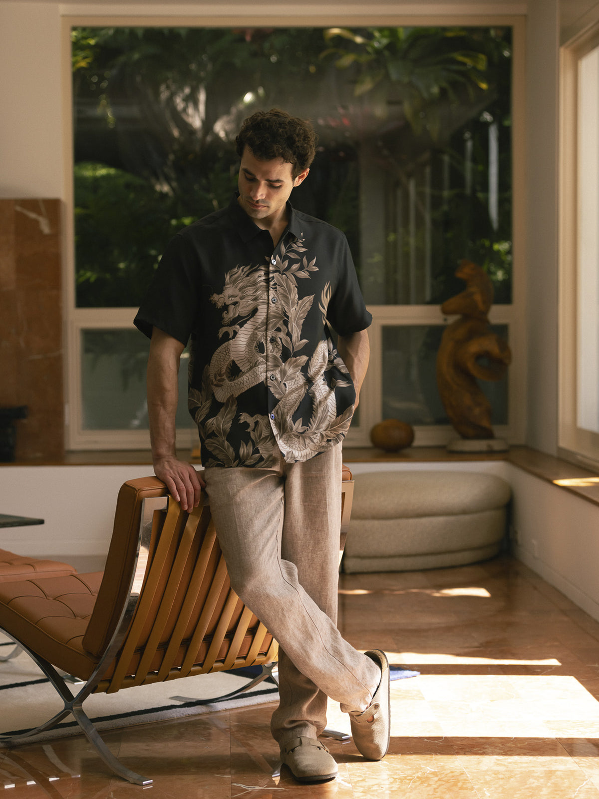 Black shirt and beige dragon-print short-sleeve shirt with beige linen pants, standing side view in both images.