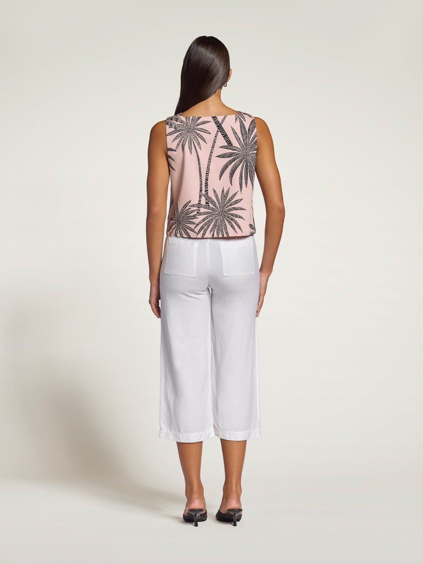 Pink palm tree-print sleeveless cropped top, back view, with white pants and black shoes.