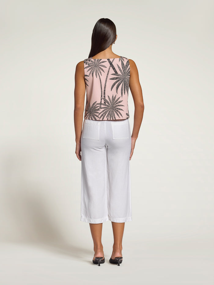 Pink palm tree-print sleeveless cropped top, back view, with white pants and black shoes.