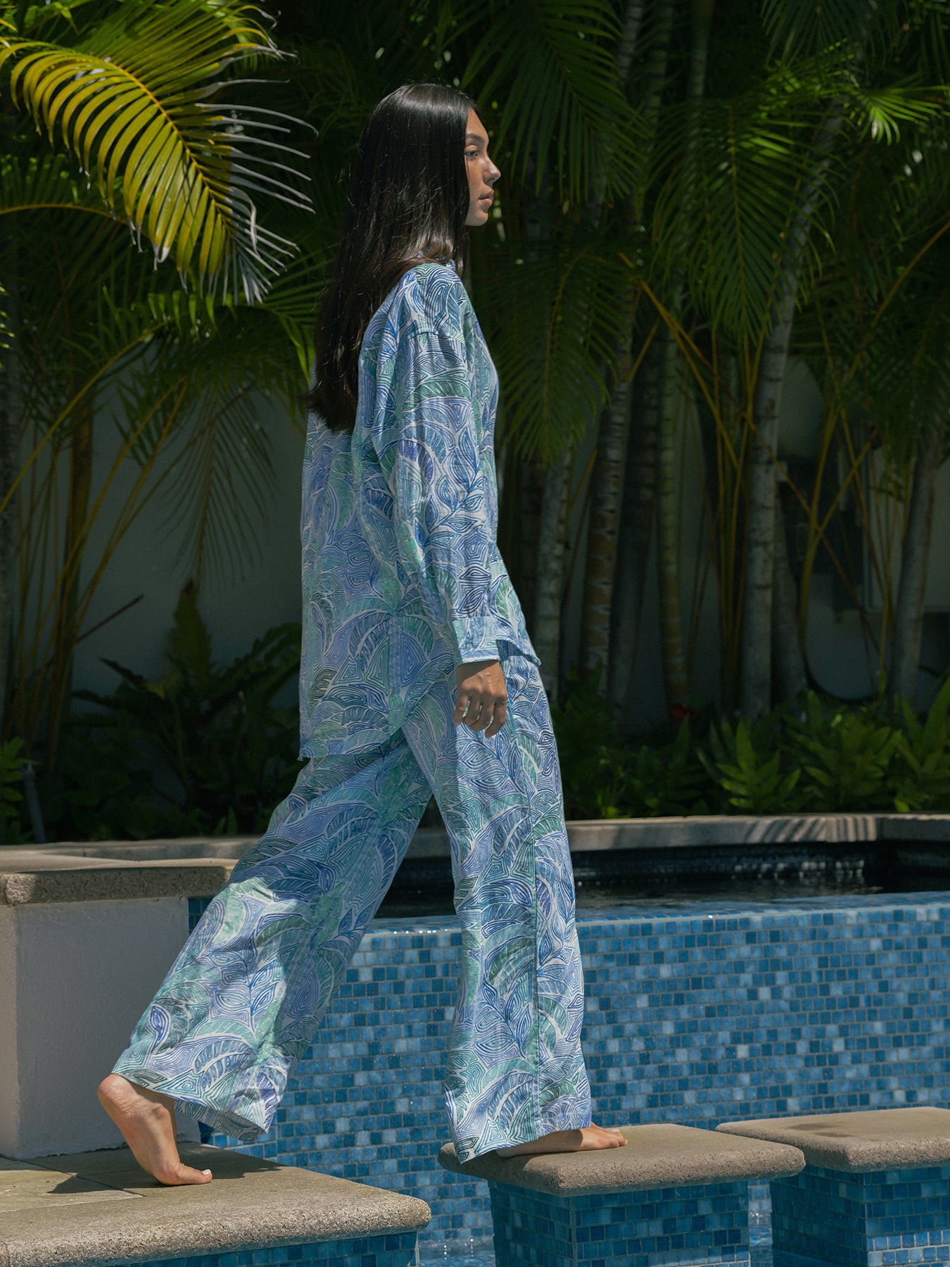 {{White and multicolor striped sleeveless top with blue patterned pajama pants, side view by pool}}.