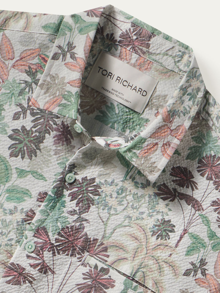 A close-up of a Tori Richard button-down shirt featuring a textured crinkle fabric and a botanical floral print in muted green, dusty rose, and brown tones on a light cream background.